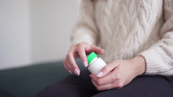A Woman Opens a Jar of Medicine, Pours a Pill Into Her Palm and Takes an Antibiotic. Colds, Flu