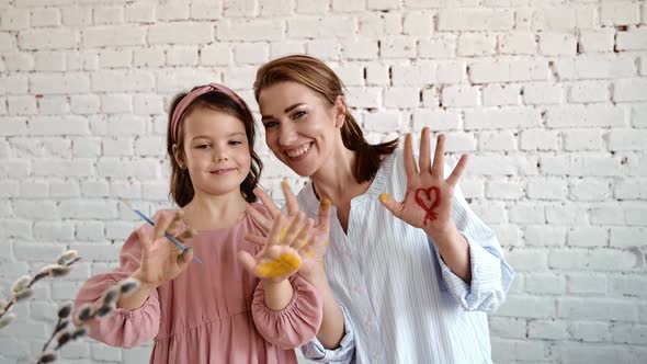 Young Mother and Brunette Daughter Overjoyed Smiling and Painting Palms with Paint