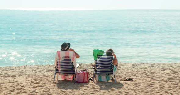 Man and Woman Use Sun Loungers While Sitting By the Ocean at the Beach alt