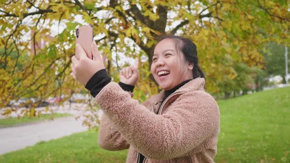 Happy Asian woman taking video call on smartphone at the park in Autumn alt