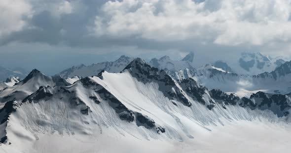 Air Flight Through Mountain Clouds Over Beautiful Snowcapped Peaks of Mountains and Glaciers alt