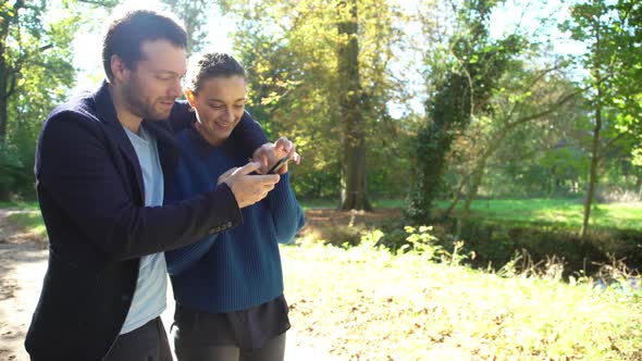Couple looking at smartphone while strolling through park alt