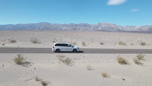 White minivan car driving along empty desert road at Death Valley, California alt