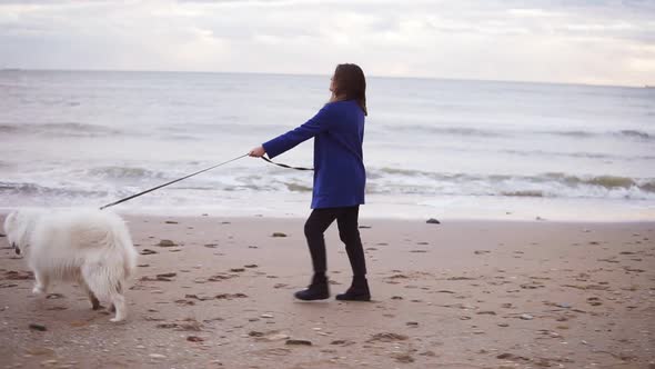 Pretty Girl Walking with Samoyed Dog on the Sand By the Sea alt