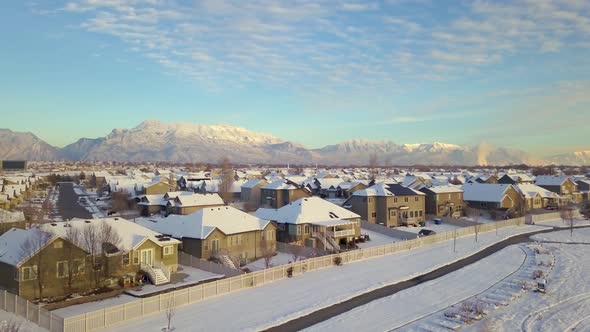 Slow, aerial pan above a picturesque neighborhood on a clear day after a snow storm with mountains i alt