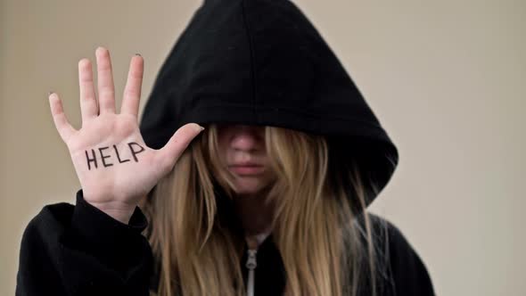Teenage Girl Covering Her Face with a Hood Shows Her Palms with the Inscription HELP ME alt