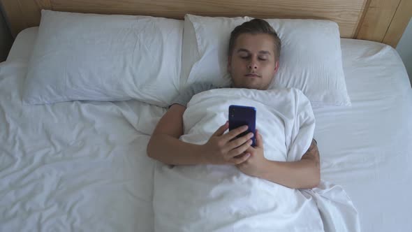 Young Handsome Man Lies in Bed Uses the Phone Before Sleeping