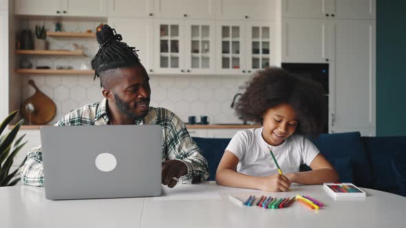 Young African American Father Working on Laptop Computer His Little Daughter Drawing with Crayons alt