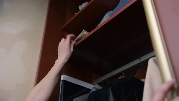 girl opens the cabinet door and hides a small stack of money on the top shelf alt