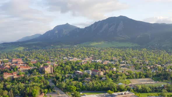 Aerial pan left of beautiful flatiron mountain vista, bright green trees, and CU Boulder campus in B alt
