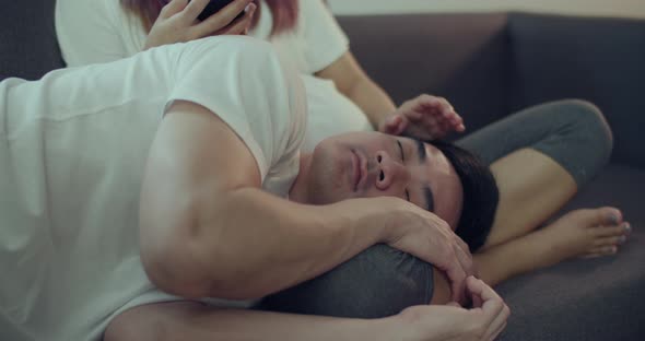 Happy Asian husband and pregnant wife spend time together on a sofa in the living room.