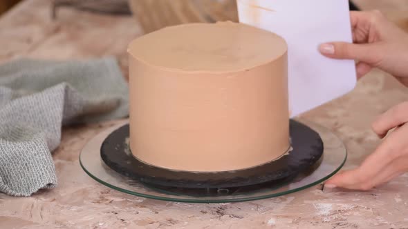 Pastry Chef Woman Is Smearing Chocolate Cream On Sponge Cake With Spatula On Rotating Cake