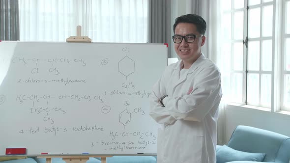 Asian Male Teacher With Glasses Crossing Arms And Smiling To Camera While Teaching Chemist At Home alt