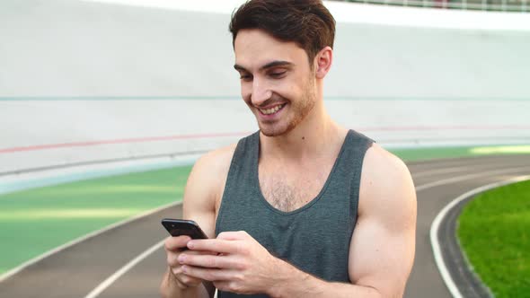Closeup Runner Standing with Smartphone on Track. Sporty Man Holding Phone alt