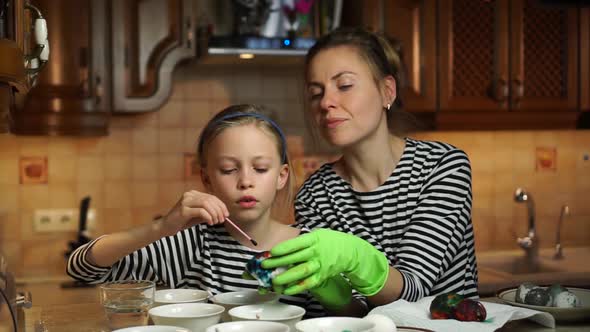 Caucasian Mother and Child Daughter in Striped Dress Decorate Easter Eggs Sitting Together at Table