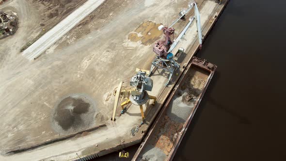 Large Harbor Cranes Onshore at the Quay Unload a River Gravel Barge Onto a Large Pile alt