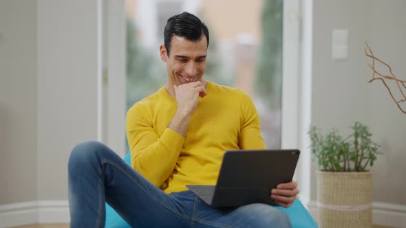 Relaxed Cheerful Middle Eastern Man Laughing Watching Movie on Tablet at Home alt