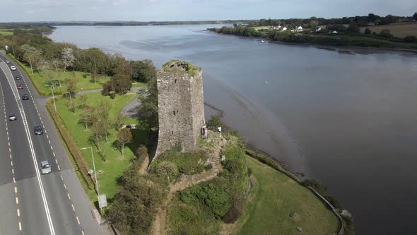 Drone shot of a busy road and old castle ruins with a wide river estuary in the background. alt