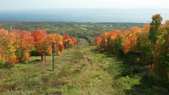 Aerial view flyover woman walking down hill with chairlifts and trees in fall colors against lake su alt