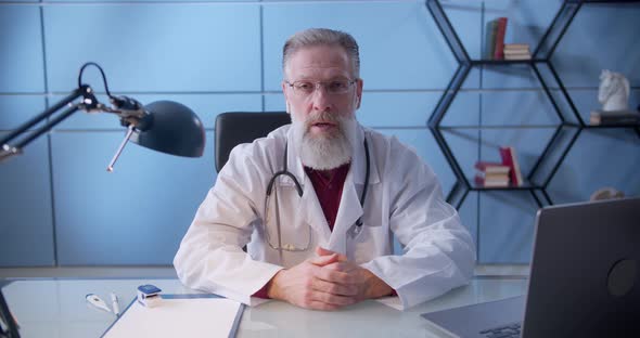 Professional Male Doctor Physician with Beard in White Medical Uniform Speaking Looking at Camera