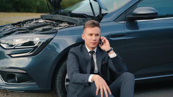 Upset Businessman Use Phone Sitting on Road Near the Broken Car alt