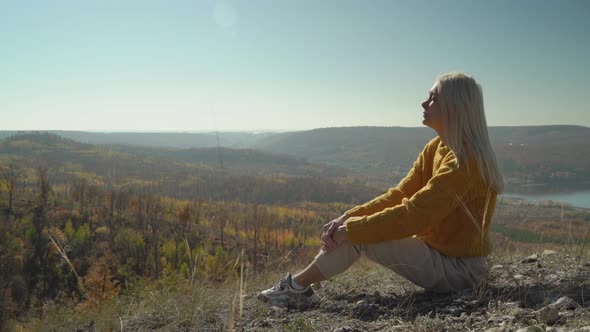Young woman sits on stones and enjoys the autumn warmth in the mountains alt