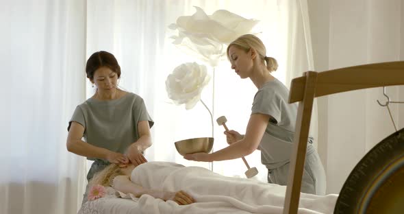 Two Female Physical Therapist Is Working with Woman in Massaging Salon, Face Massage and Tibetan alt