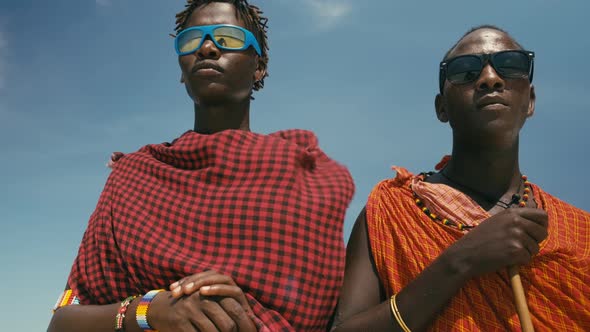 Young Masai Tribe Members in Red Dresses and Sunglasses Standing on Sand Beach of Indian Ocean