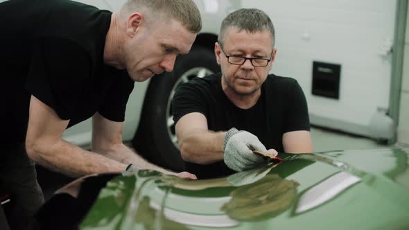 Two Men are Focused on the Process of Vinyl Wrapping a Car Using Plastic Cards