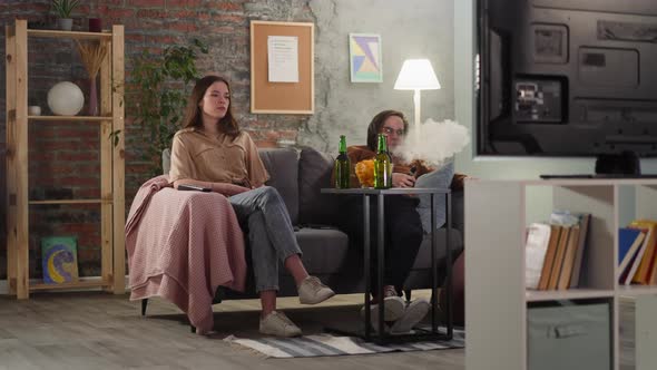 Man Smokes Vape Sitting with Woman at Football Game in Flat alt