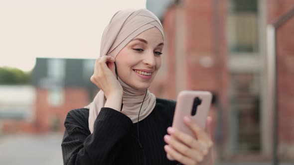 Young Muslim Woman Listening to Music While Walking Down a City Street alt