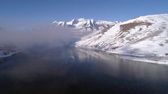 Aerial view flying backwards viewing winter landscape surrounding lake alt