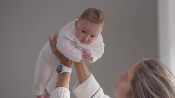 Cheerful Caucasian Infant Girl in Hands of Young Mother Talking in Slow Motion alt