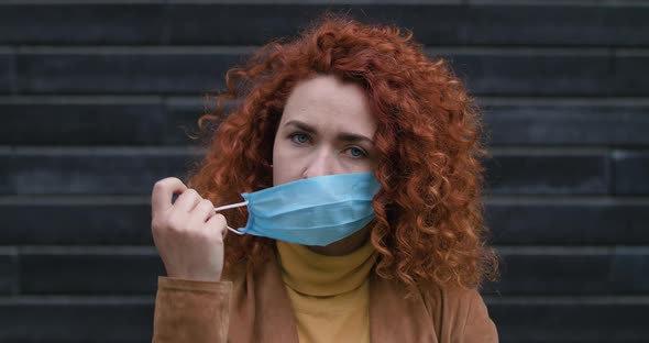 Beautiful Young Red-haired Caucasian Woman Removes the Medical Mask Looking Into the Camera, End of alt