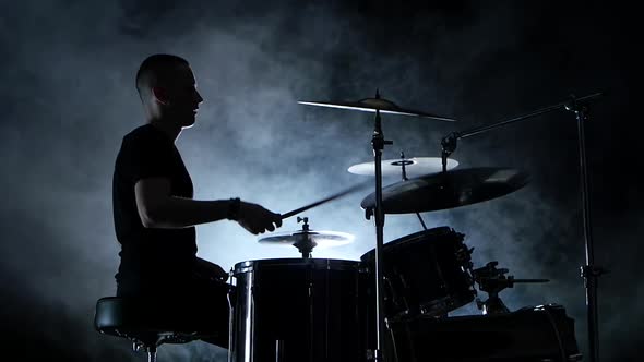Energetic Musician Plays Good Music on Drums, Black Smoky Background, Side View, Silhouette alt