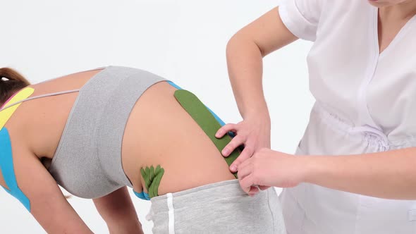Physiotherapist sticks kinesio tapes to the small of the back of female patient, kinesiology taping alt
