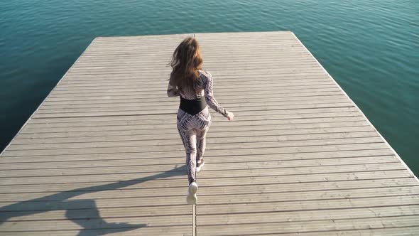 girl athlete with a beautiful figure runs on the pier of the lake. Slow motion. Top view alt