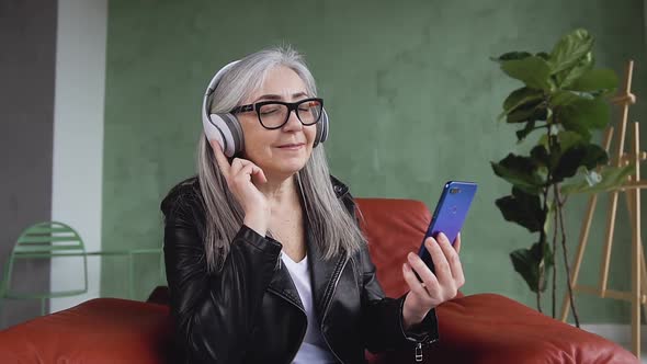 Trendy Retired Woman in Headphones which Sitting on Armchair and Listening the Beautiful Songs alt
