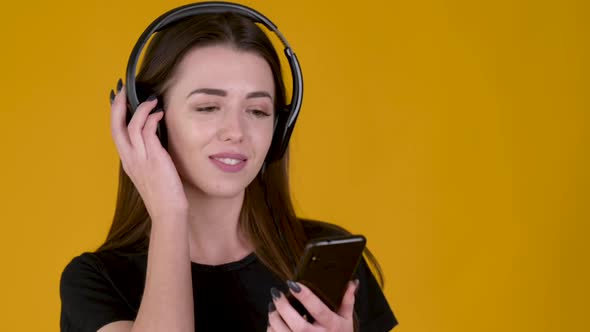 Young girl with headphones listens to music and dances isolated on yellow background.