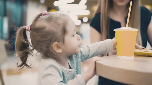 Mom Feeds a Little Daughter with a Fork They Sit in a Cafe alt