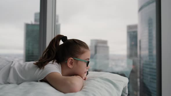 Cute Teenage Girl Relaxes on a Comfortable Bed Looking at the City From a Height alt