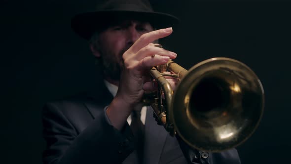 Male Musical Artist Playing Trumpet in Rays of Spotlight on Dark Background Front View alt