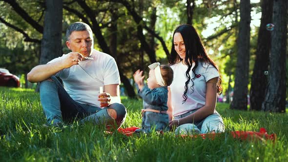 happy family with baby girl spending time in summer park blowing soap bubbles alt