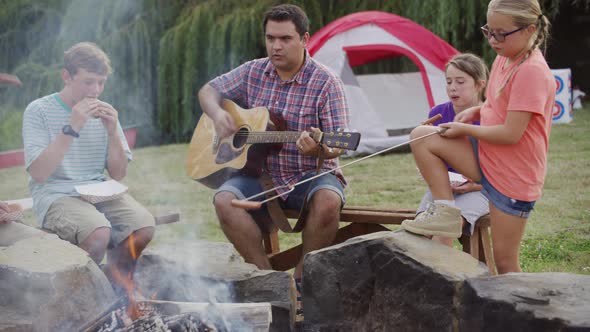 Kids at summer camp by campfire with leader playing guitar