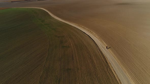 The SUV Moves Between the Fields Bypassing a Woman Pedestrian