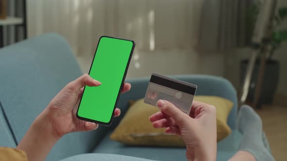 Asian Woman Sitting On Couch In Living Room Using Smartphone With Mock Up Green Screen Display alt