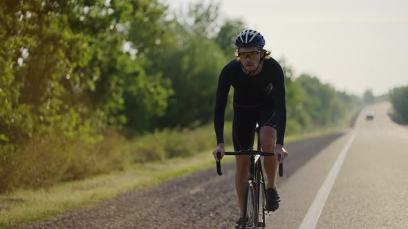 Male Cyclist in Helmet Rides Bicycle Along the Track Overcomes Way Up alt