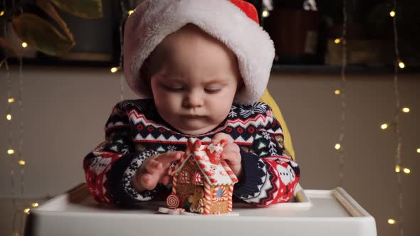 Cute Serious Little Baby Boy in Santa Hat Playing with Toy Gingerbread House alt