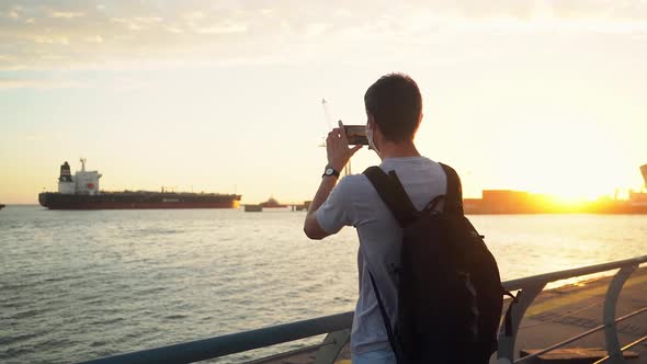 Man With Backpack Taking Photo Of A Ship Moored At Quiet Ocean At The Port Of Puerto Ingeniero White alt