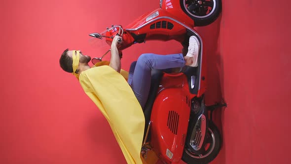 Crazy Man Driving a Moped Scooter in Cape and Mask Party in the Role of a Super Hero, Isolated alt